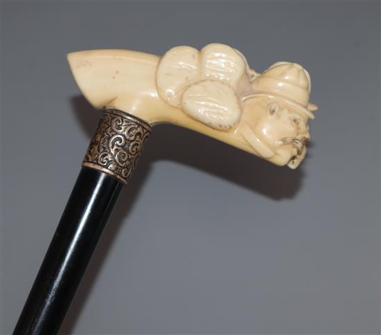 A lacquered walking cane with silver collar and carved ivory handle, in the shape of two warped faces length 90cm